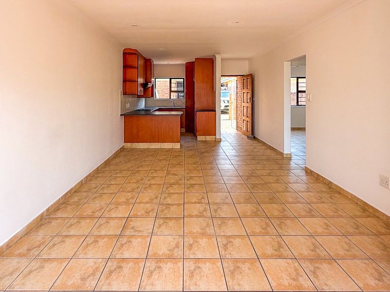 An open-plan living and kitchen area featuring tiled flooring, wooden cabinetry, and built-in kitchen appliances, offering a functional and versatile layout.
