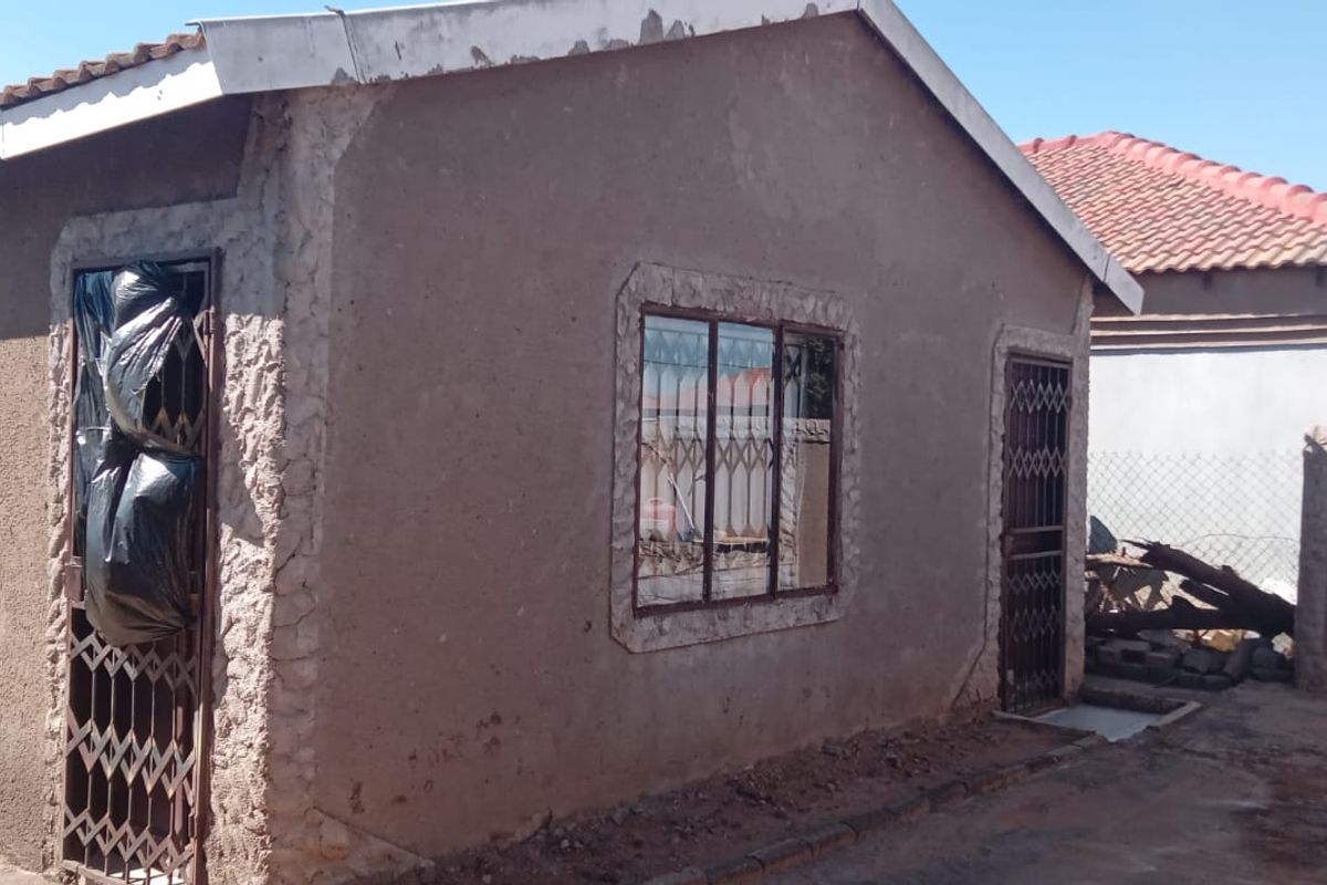 Exterior view of a residential property showing plastered walls, metal security gates, and a tiled roof, requiring maintenance and finishing work.