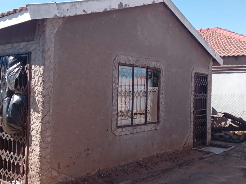 Exterior view of a residential property showing plastered walls, metal security gates, and a tiled roof, requiring maintenance and finishing work.