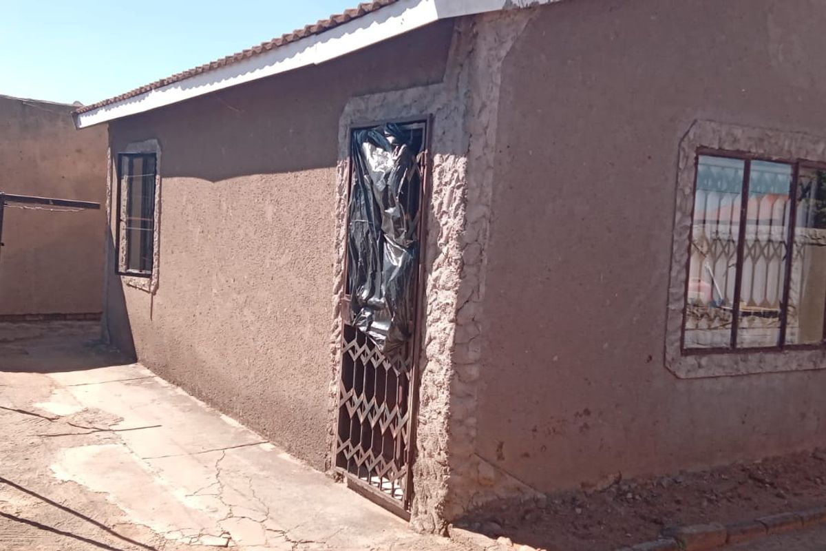 Rear exterior view of the property showing plastered walls, security gates, and concrete paving in need of maintenance.