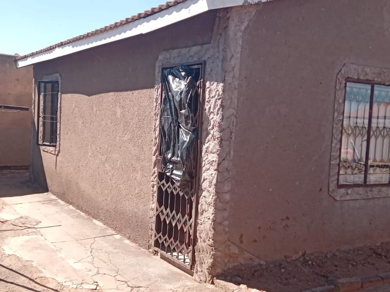 Rear exterior view of the property showing plastered walls, security gates, and concrete paving in need of maintenance.