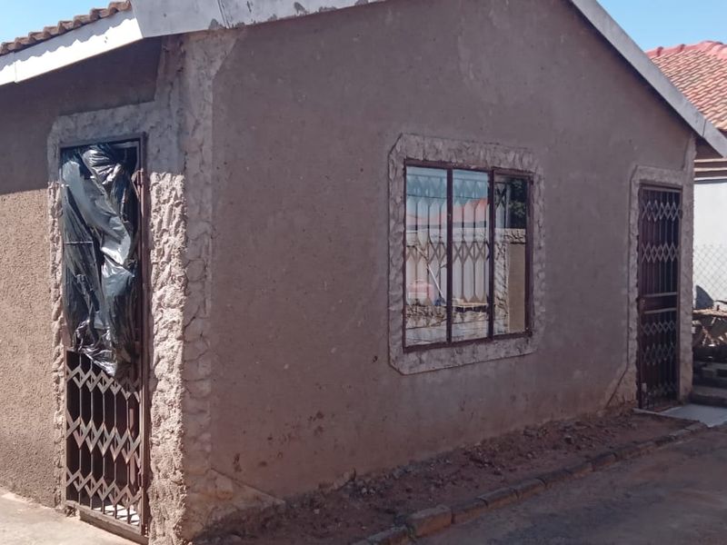 Rear view of a residential house featuring textured plaster walls, metal security gates, and a tiled roof, requiring exterior maintenance and finishing.