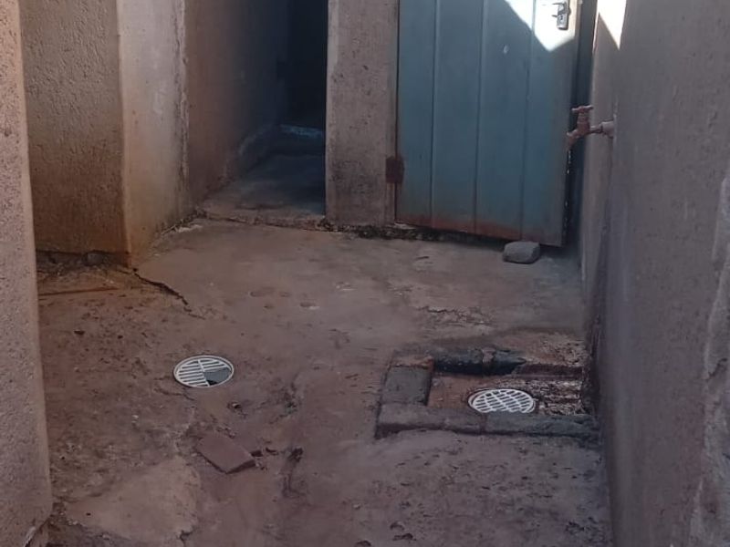 An exterior utility area featuring concrete flooring with drainage, an external tap, and access to a secondary door.