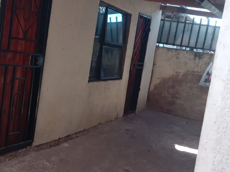 A covered outdoor patio area featuring exposed timber rafters, concrete flooring, and security gates, requiring maintenance and cosmetic upgrades.
