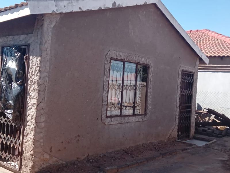 Exterior view of a single-story house featuring a tiled roof, security gates, and plastered walls, showing signs of wear and maintenance requirements.