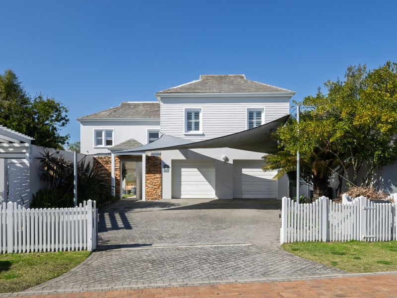 A well-maintained double-story home featuring a paved driveway, double garage, stone accents, and a classic white picket fence.