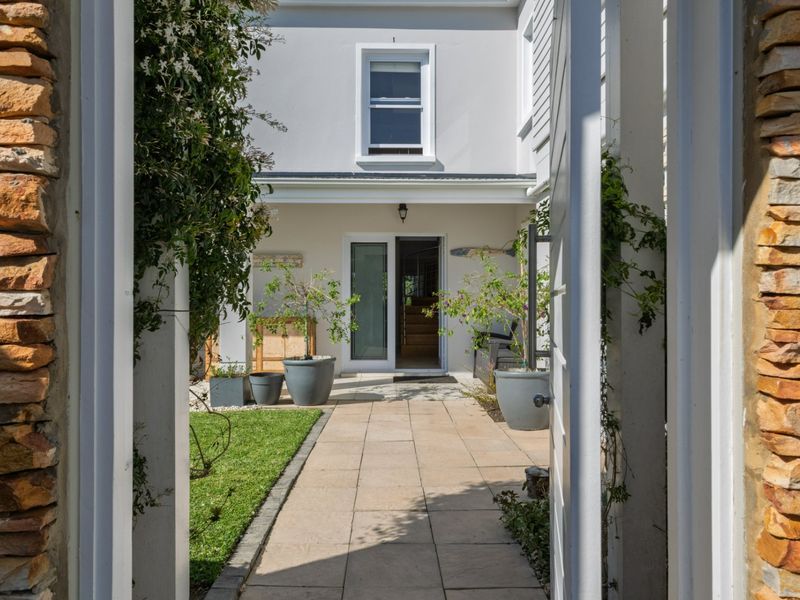 A view through a stone-clad entrance gate into a well-maintained rear courtyard with a paved walkway and landscaped garden area.