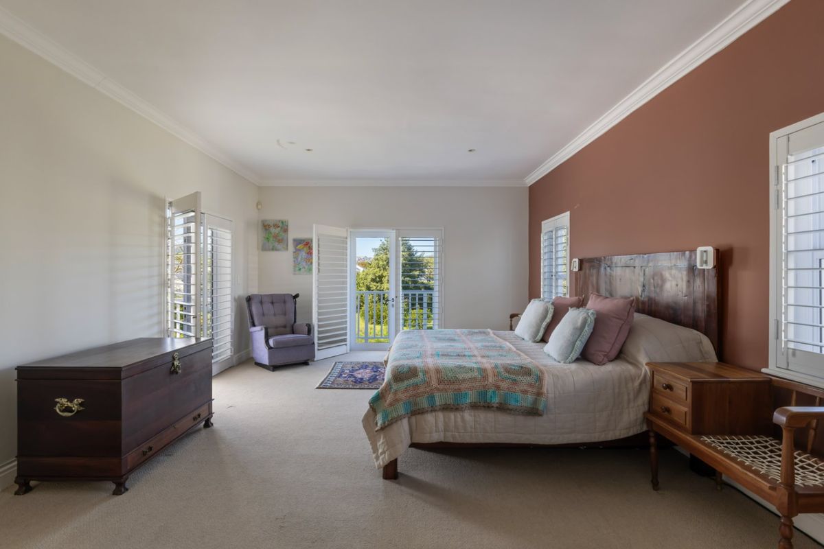 Spacious bedroom featuring neutral carpeting, crown molding, plantation shutters, and direct access to a private balcony through glass french doors.