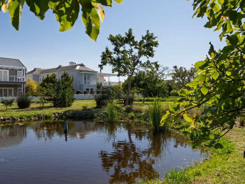 A scenic view of a well-maintained garden featuring a tranquil pond, lush greenery, and a white picket fence surrounding the property.