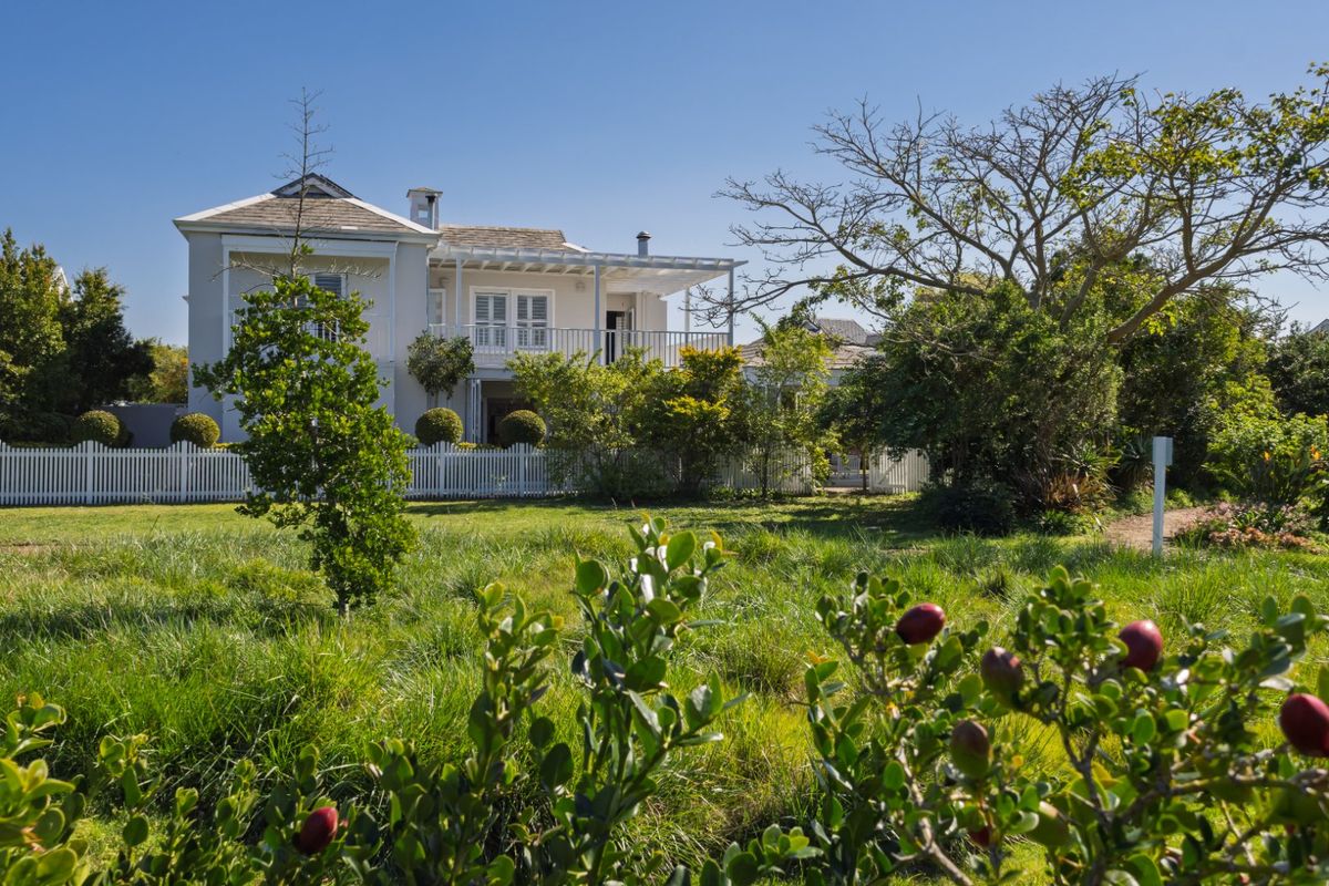 A charming two-story residence featuring a covered patio, upper balcony, and a classic white picket fence set within a lush, landscaped garden.