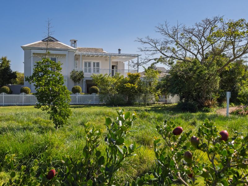 A charming two-story residence featuring a covered patio, upper balcony, and a classic white picket fence set within a lush, landscaped garden.