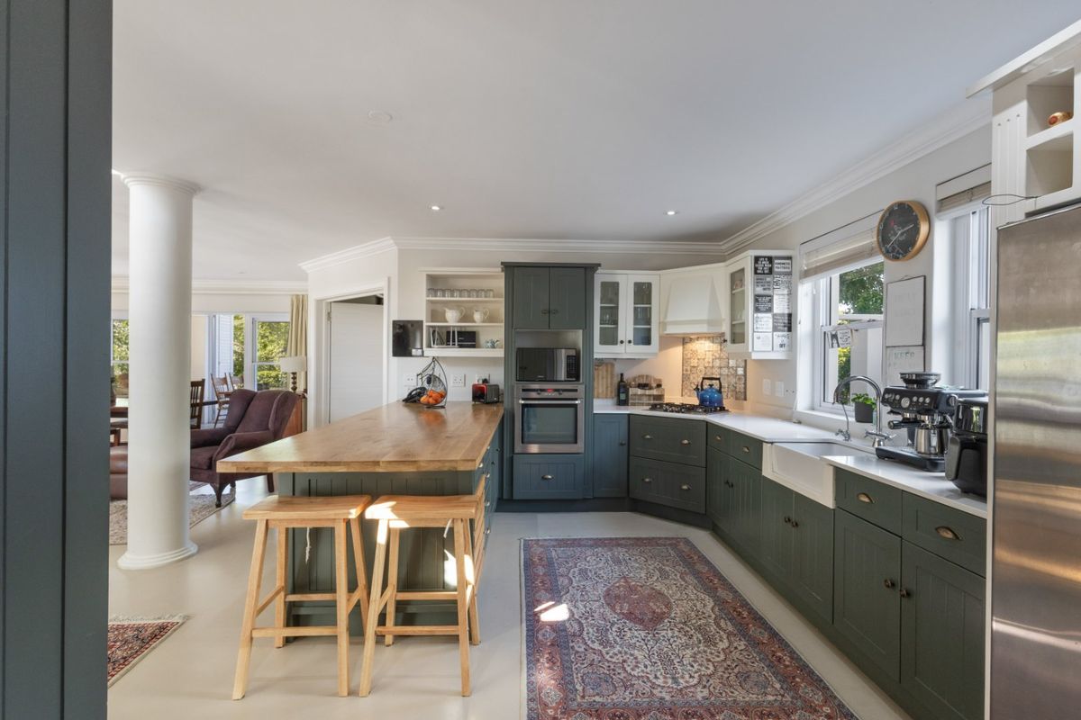 Modern kitchen featuring dark green shaker cabinetry, a large wooden-topped island, butler sink, and integrated appliances, seamlessly flowing into the adjacent living area.