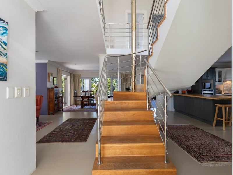 Open plan living area featuring a central timber staircase with stainless steel balustrade, leading to a modern kitchen with dark cabinetry and timber countertops.