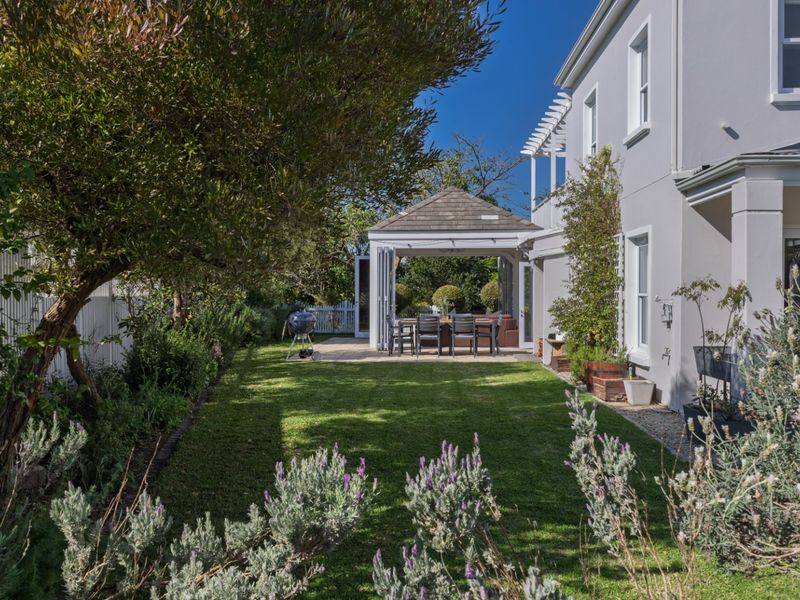 A well-maintained rear garden featuring a lush lawn, landscaped borders, and a covered patio area with a pergola, perfect for outdoor entertaining.