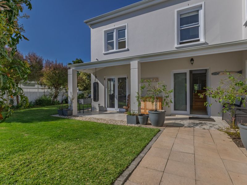A well-maintained rear exterior view featuring a covered patio, paved walkway, manicured lawn, and white picket fencing.
