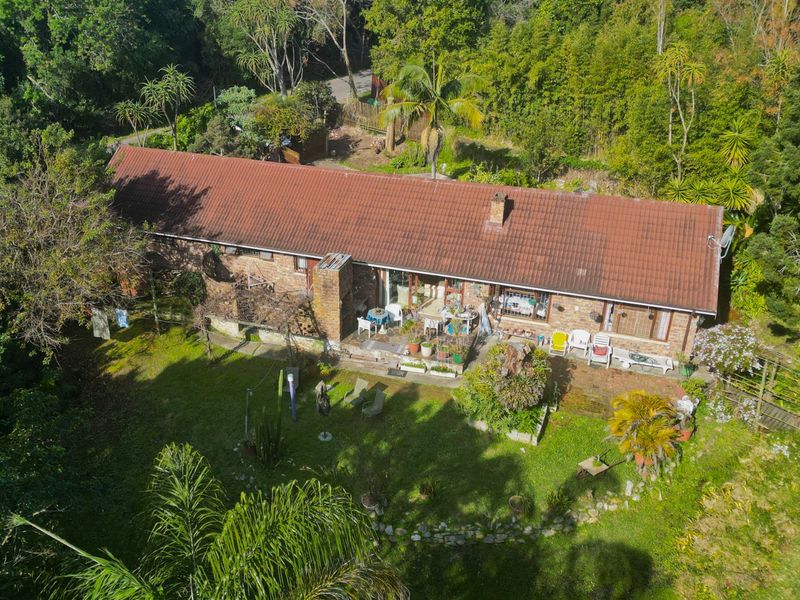 Aerial view of a single-story brick house with a tiled roof, featuring a rear patio and established garden surroundings.