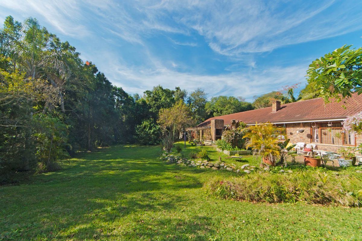 Spacious rear garden featuring a brick facade house, tiled roof, stone retaining wall, and a built-in outdoor braai area.