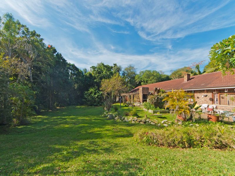 Spacious rear garden featuring a brick facade house, tiled roof, stone retaining wall, and a built-in outdoor braai area.