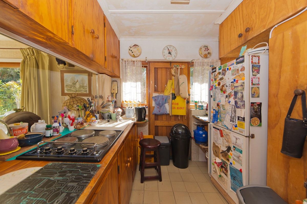 A dated kitchen featuring wooden cabinetry, an electric hob, and tiled flooring, in need of cosmetic updates to improve its overall condition and aesthetic appeal.