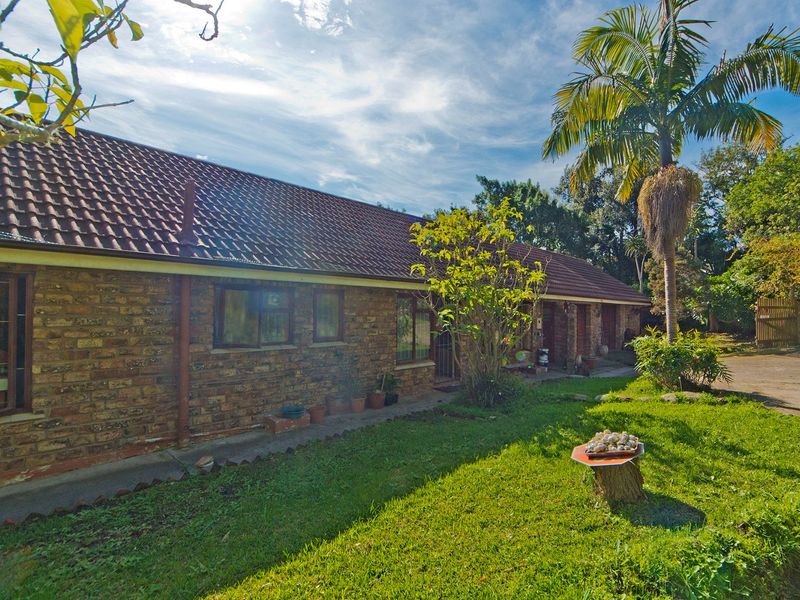 A view of the rear exterior of the house featuring a face brick facade, tiled roof, and a surrounding garden area.