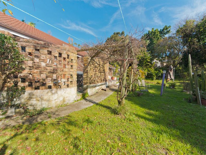 Rear garden area featuring a decorative brick screen wall, a wooden pergola structure, and a concrete pathway leading along the side of the house.