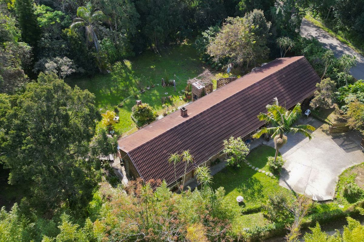 Aerial view of a residential property featuring a long tiled roof, established garden, driveway, and outdoor fireplace area.