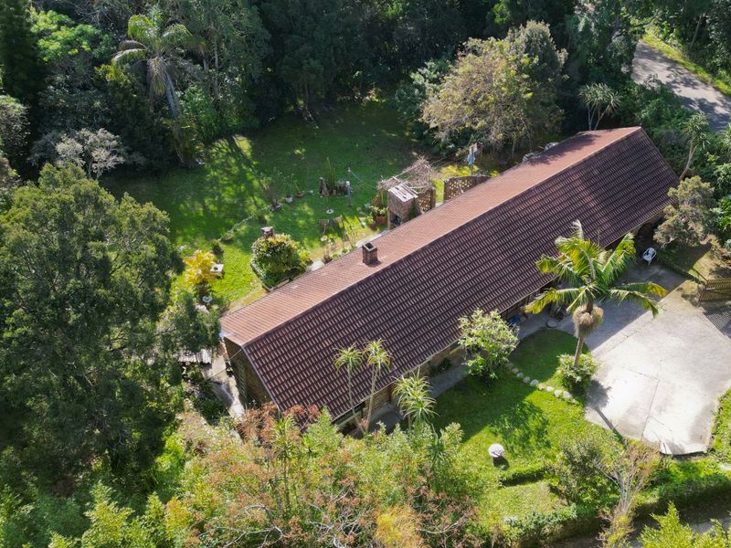 Aerial view of a residential property featuring a long tiled roof, established garden, driveway, and outdoor fireplace area.