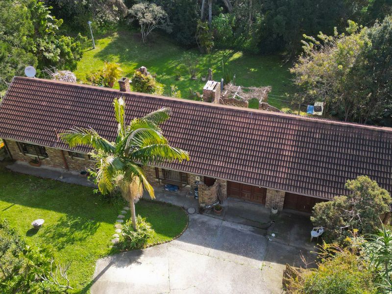 Aerial view of a single-story brick house with a tiled roof, double garage, concrete driveway, and surrounding garden area.