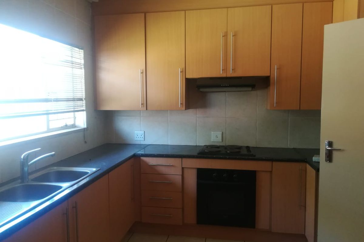 A functional kitchen featuring light wood cabinetry, dark countertops, a built-in oven, electric hob, and a double sink with tiled backsplash.