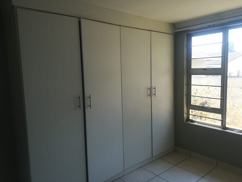 A clean, empty bedroom featuring neutral tiled flooring and floor-to-ceiling built-in cupboards with modern handles, complemented by a window with security bars.