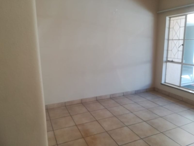 An empty living area featuring neutral tiled flooring and a window fitted with security bars.