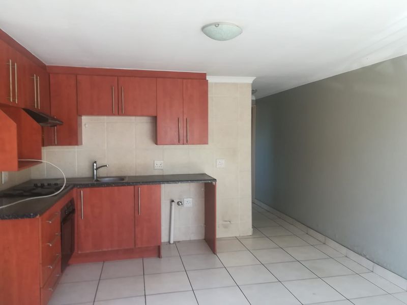 A functional kitchen featuring wood-tone cabinetry, dark laminate countertops, built-in oven and hob, and tiled flooring, offering a clean and practical workspace.