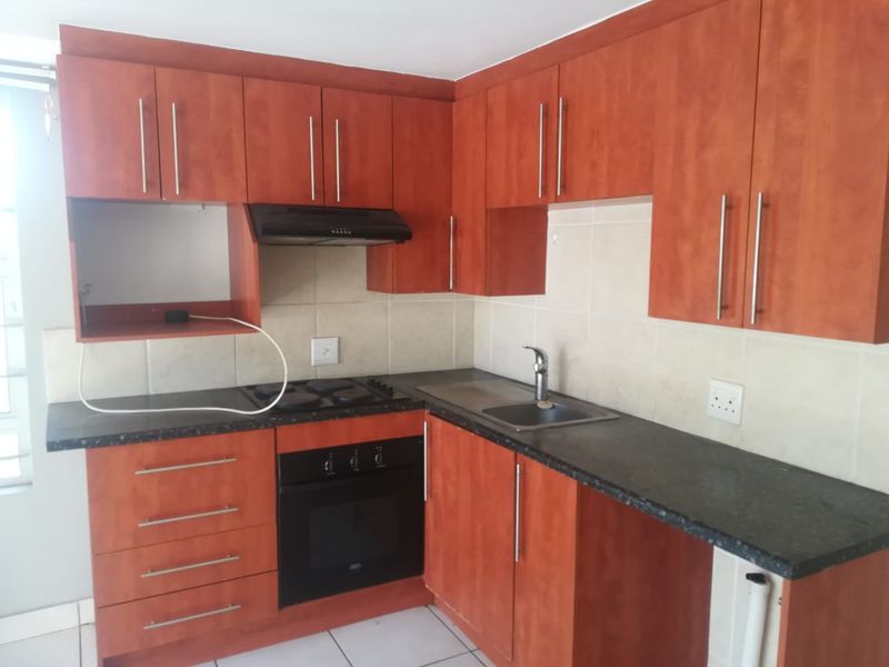 A functional kitchen featuring wood-tone cabinetry, dark laminate countertops, built-in oven, electric hob, extractor fan, and a stainless steel sink with tiled splashback.