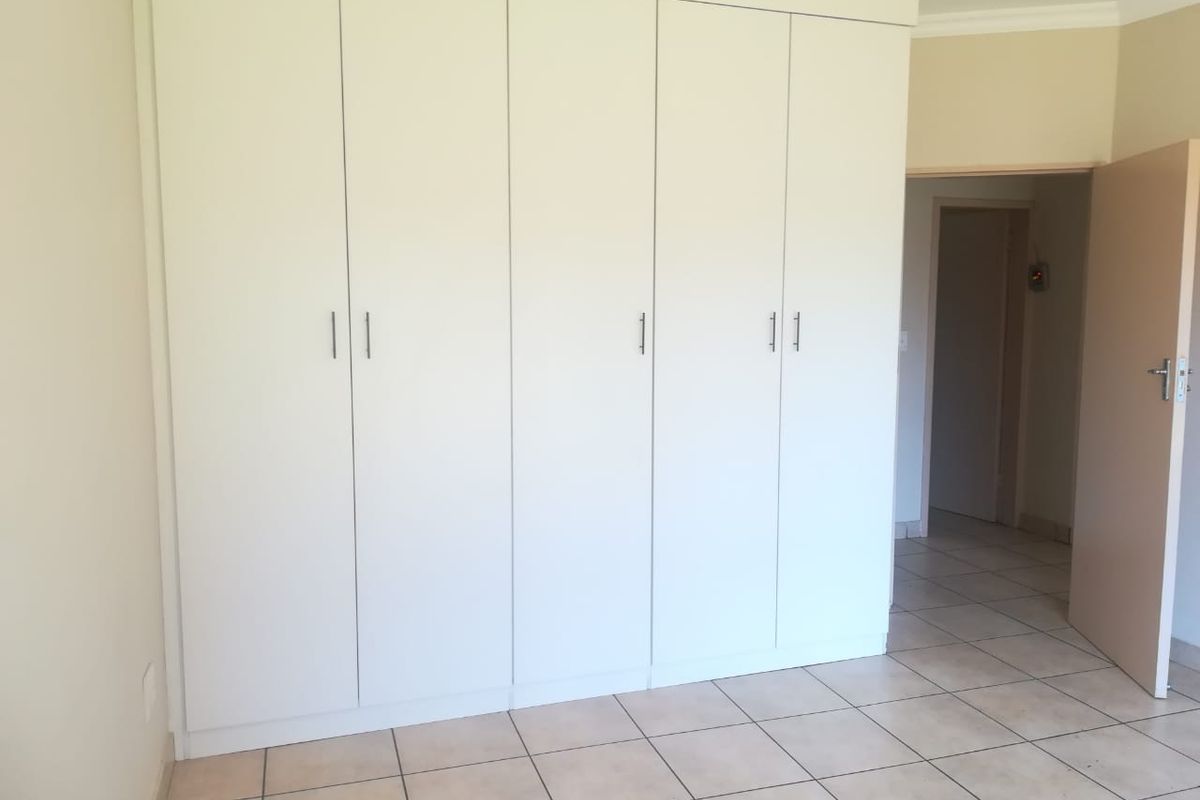 A clean, empty bedroom featuring neutral tiled flooring and ample built-in cupboard storage space.