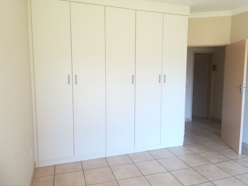 A clean, empty bedroom featuring neutral tiled flooring and ample built-in cupboard storage space.