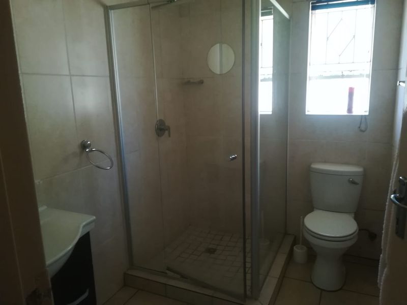 A functional bathroom featuring a glass-enclosed shower, a standard toilet, and a vanity basin with neutral wall and floor tiling.