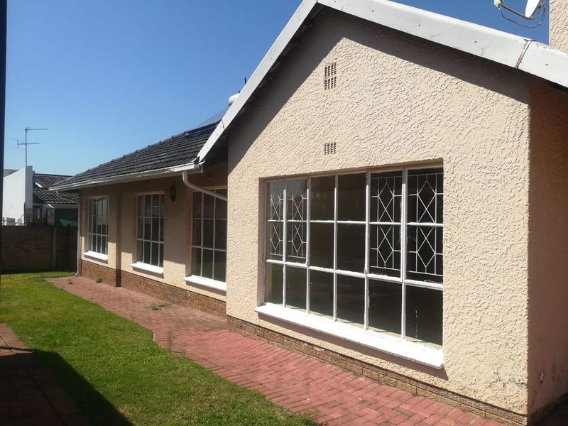 Rear exterior view of the house featuring a paved walkway, plastered facade, and large windows with security bars.