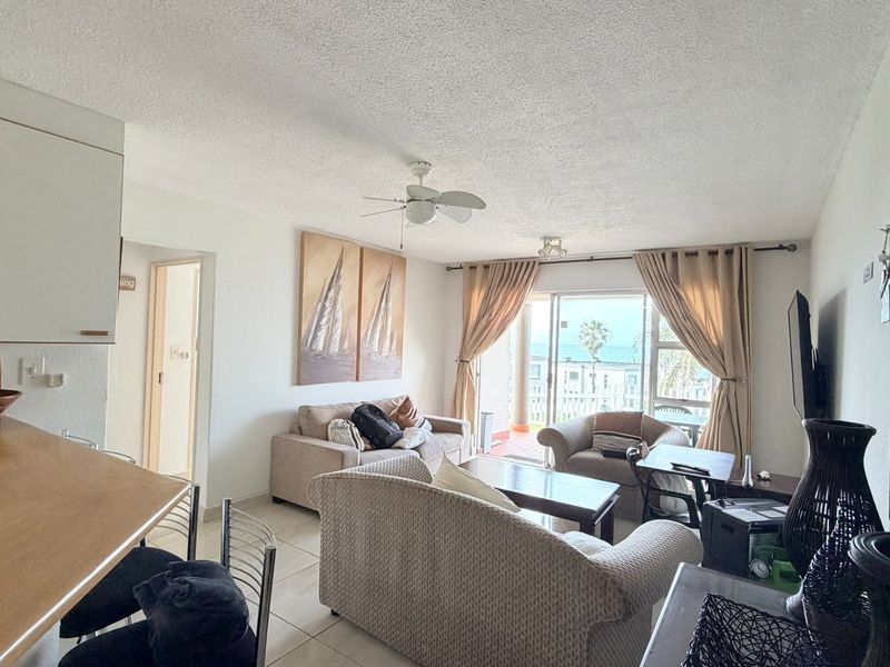 Open plan living and kitchen area featuring tiled floors, a ceiling fan, and sliding glass doors leading to a balcony with ocean views.