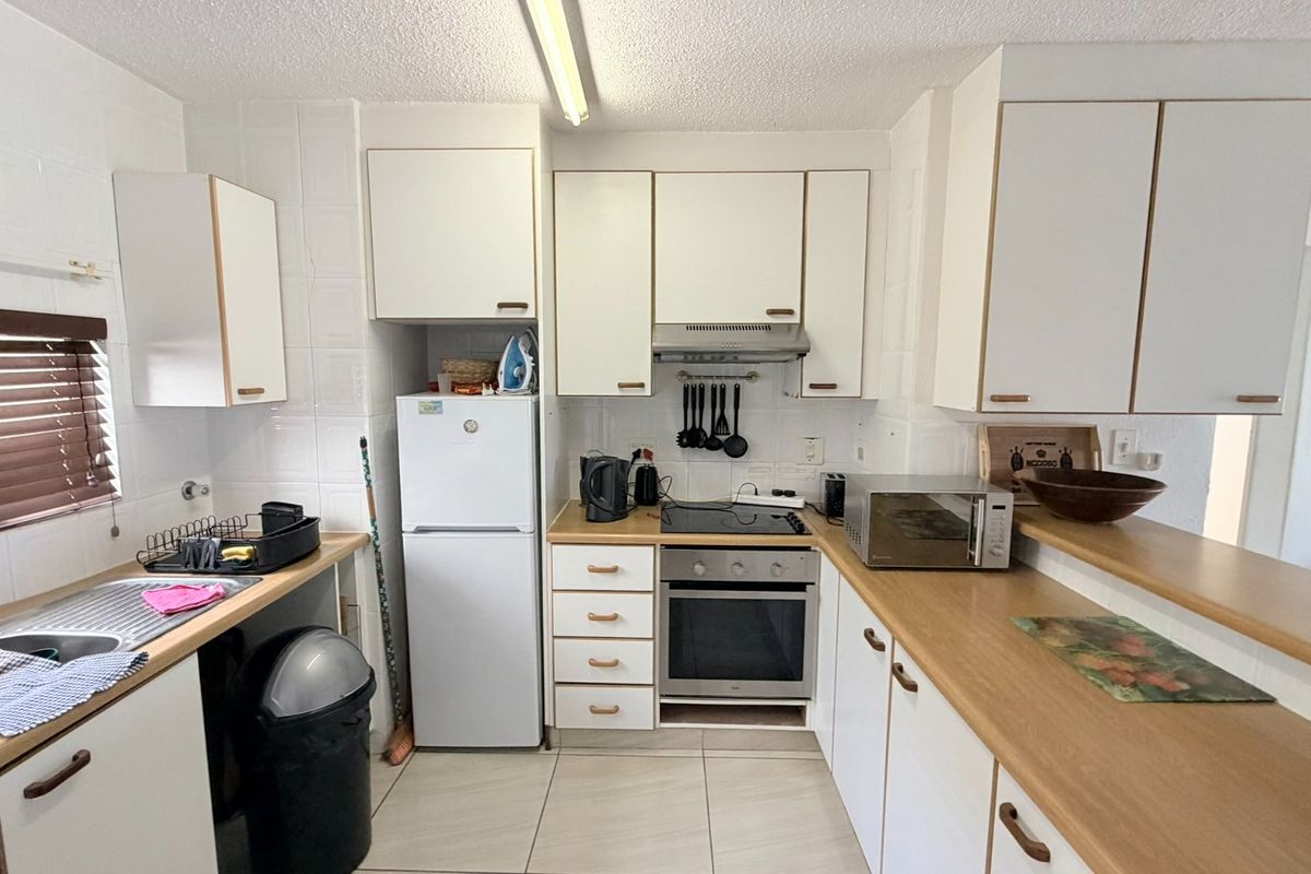 Functional kitchen featuring white cabinetry, laminate countertops, built-in oven, electric hob, and tiled splashbacks, offering a practical layout for daily meal preparation.