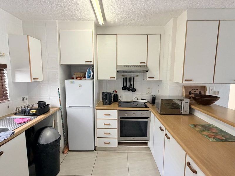 Functional kitchen featuring white cabinetry, laminate countertops, built-in oven, electric hob, and tiled splashbacks, offering a practical layout for daily meal preparation.