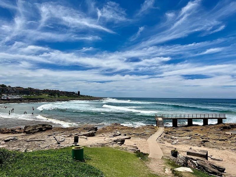 Scenic coastal view featuring a concrete walkway leading to a pier overlooking the ocean and rocky shoreline.