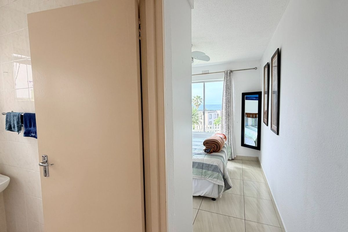 A bedroom featuring tiled flooring and a sliding glass door with ocean views, adjacent to a small bathroom area with a pedestal basin.