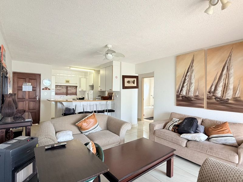 Open-plan living and kitchen area featuring tiled flooring, a breakfast bar, and a ceiling fan, offering a functional layout for modern apartment living.