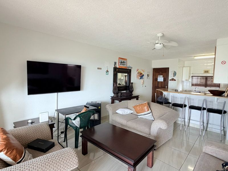 Open-plan living area featuring tiled flooring, a ceiling fan, and a breakfast bar connecting to the kitchen space.
