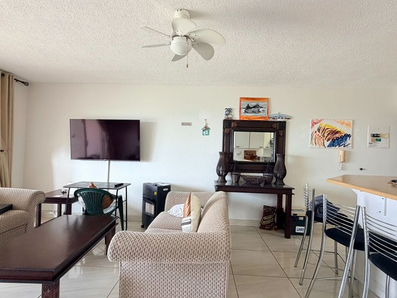 Open plan living area featuring tiled flooring, a ceiling fan, and a breakfast bar connecting to the kitchen space.
