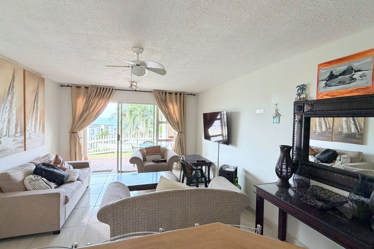 A bright living room featuring tiled flooring, a ceiling fan, and large sliding glass doors that provide access to an outdoor patio area.