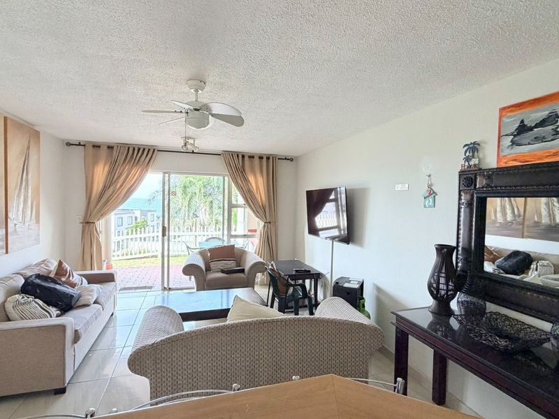A bright living room featuring tiled flooring, a ceiling fan, and large sliding glass doors that provide access to an outdoor patio area.