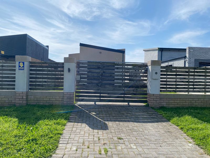 Front entrance view featuring a paved driveway, masonry boundary wall, and a timber slat sliding gate with integrated security features.