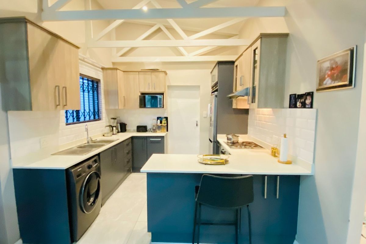 Modern kitchen featuring two-tone cabinetry, quartz countertops, subway tile backsplash, and exposed white roof trusses, creating a bright and functional culinary space.