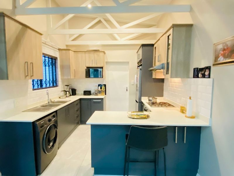 Modern kitchen featuring two-tone cabinetry, quartz countertops, subway tile backsplash, and exposed white roof trusses, creating a bright and functional culinary space.
